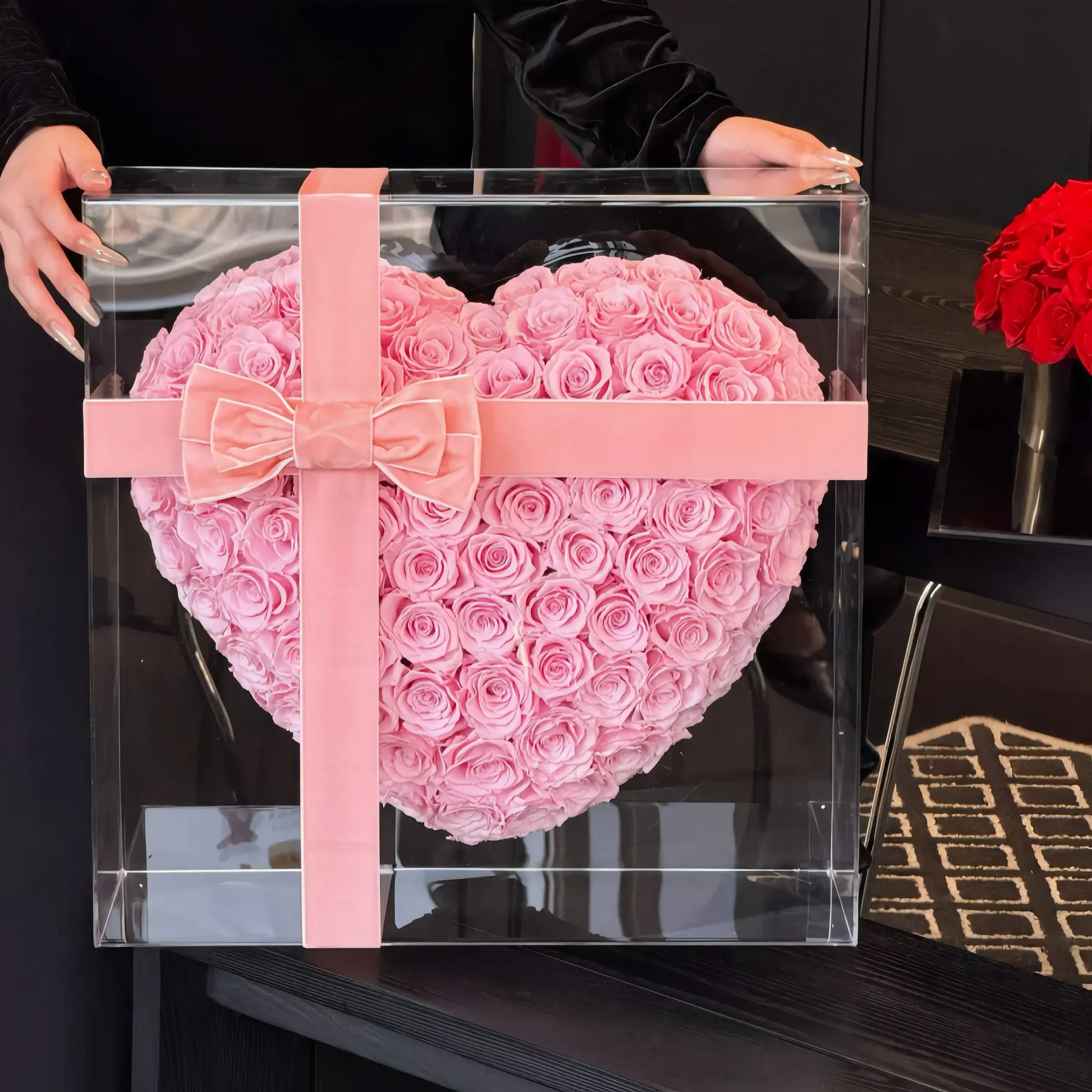 LULU ROSÉE 99 3D heart rose box light pink roses in a clear box with a pink ribbon, held by a person.