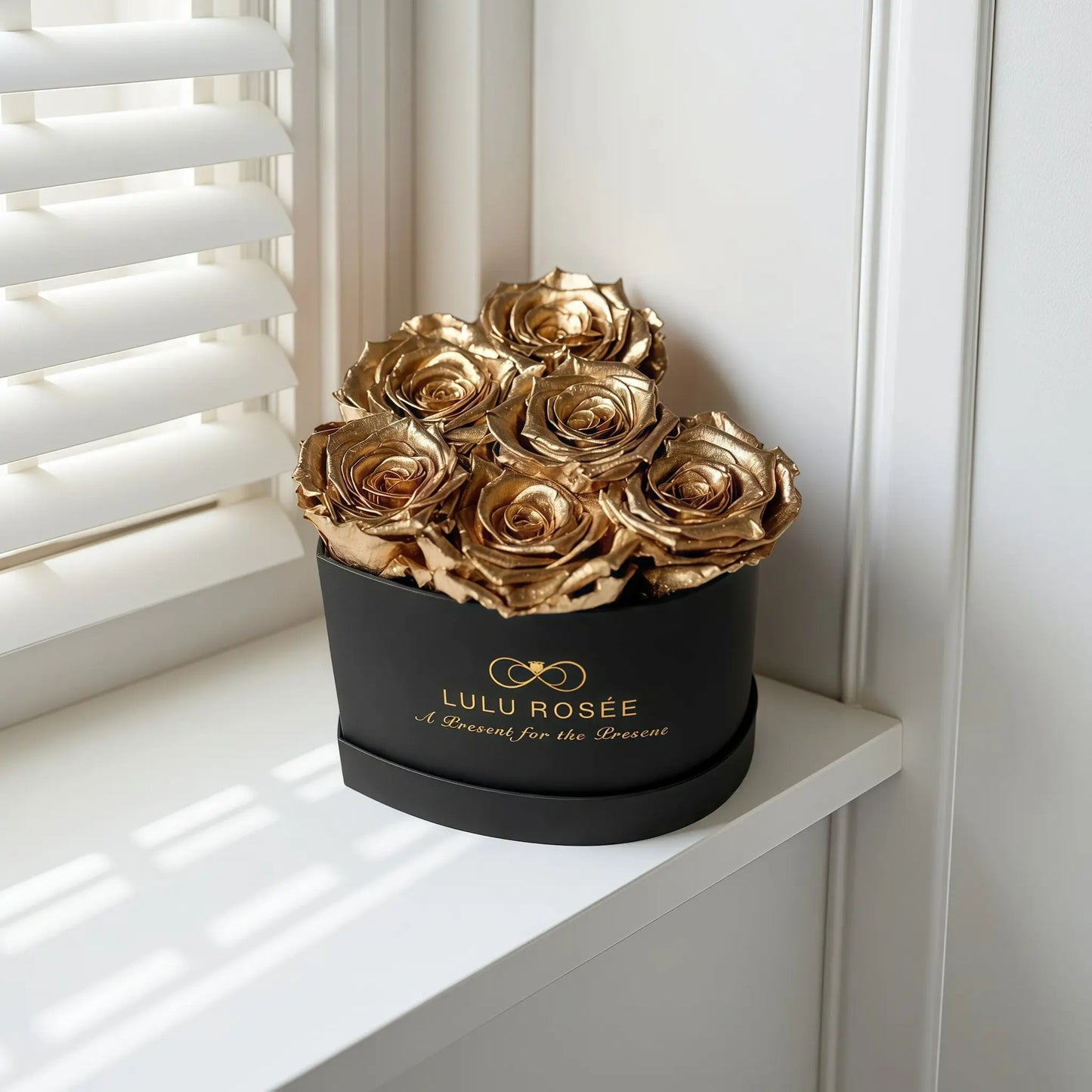 LULU ROSÉE baby heart box gold roses black classic box on a white surface near a window