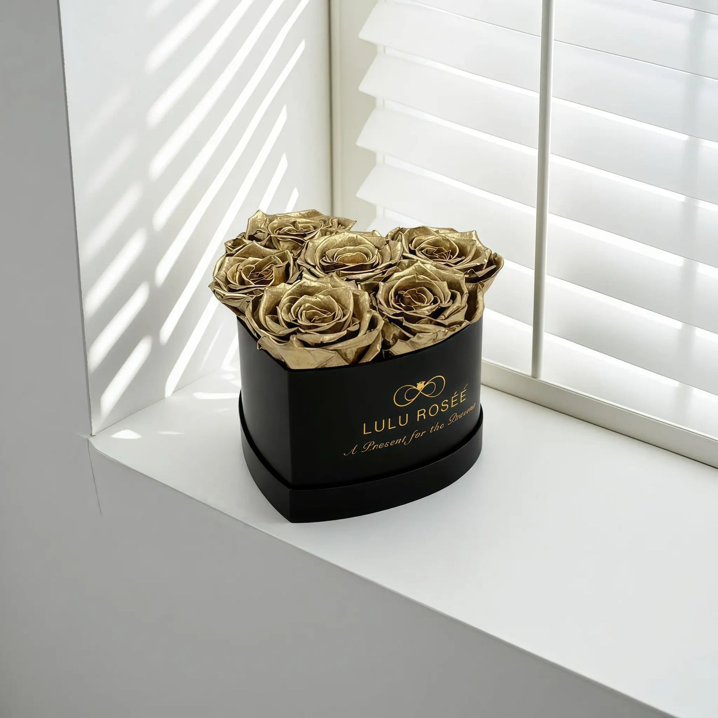 LULU ROSÉE baby heart box gold roses black classic box on a white surface with blinds in the background