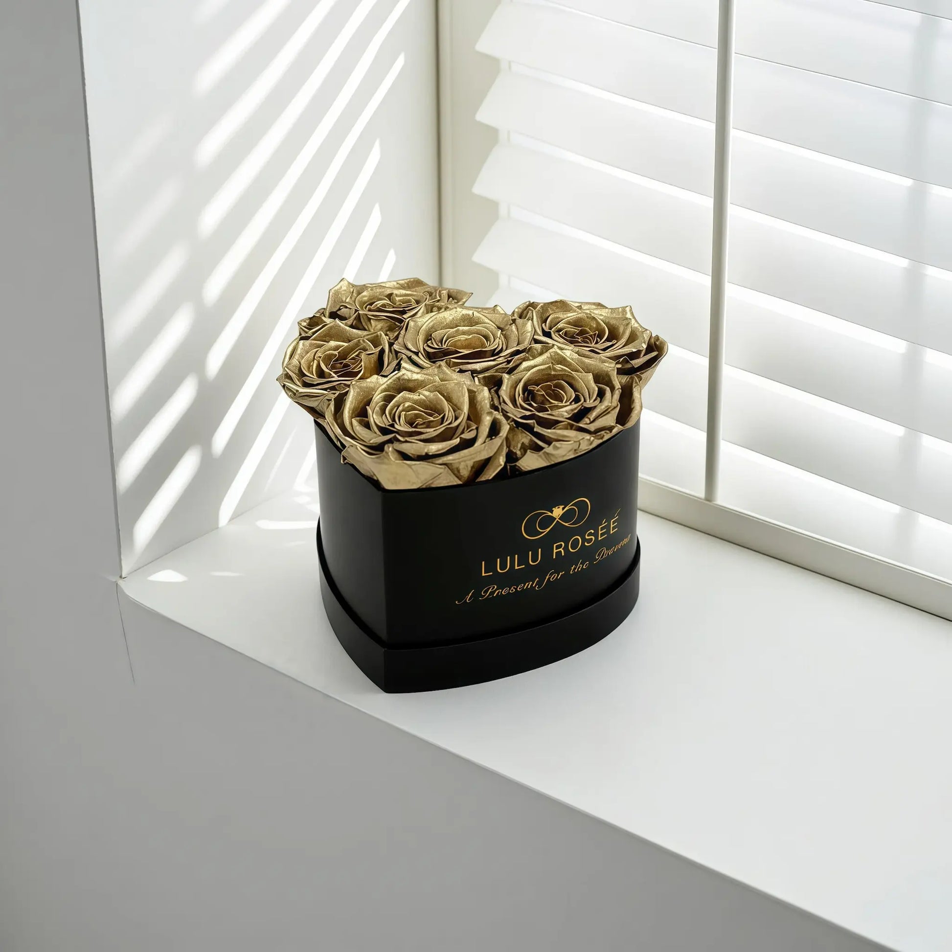 LULU ROSÉE baby heart box gold roses black classic box on a white surface with blinds in the background
