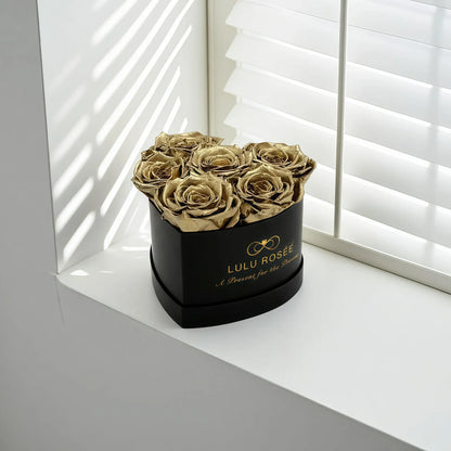 LULU ROSÉE baby heart box gold roses black classic box on a white surface with blinds in the background