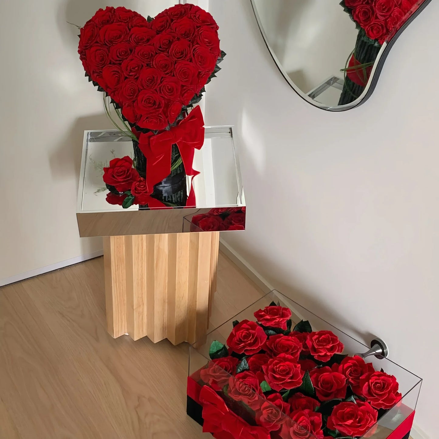 Heart-shaped arrangement of red roses on a wooden stand with a mirror reflection.