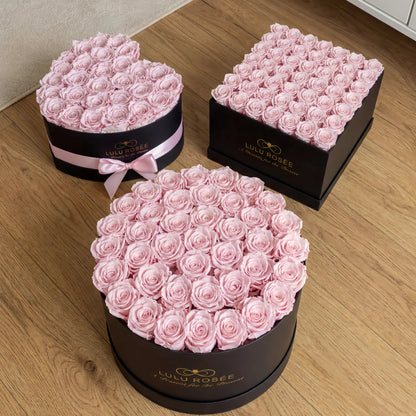 Three black boxes filled with pink roses on a wooden floor, branded 'Lulu Rosee'.