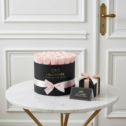 LULU ROSÉE large round box light pink roses black classic box on a marble table with a white door in the background