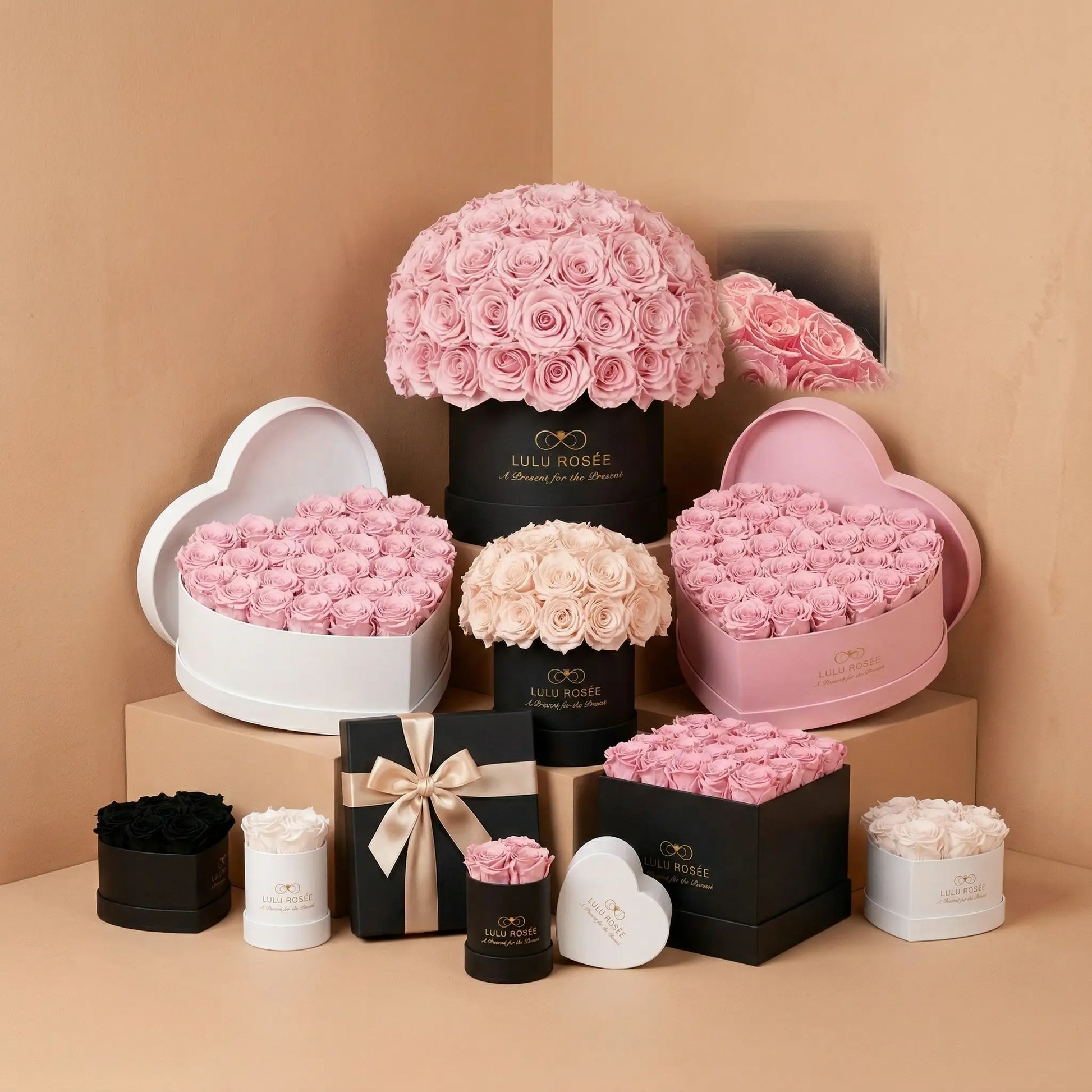 A collection of LULU ROSÉE preserved rose boxes including heart box, round box, and dome box arranged on a beige background