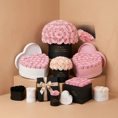 A collection of LULU ROSÉE preserved rose boxes including heart box, round box, and dome box arranged on a beige background