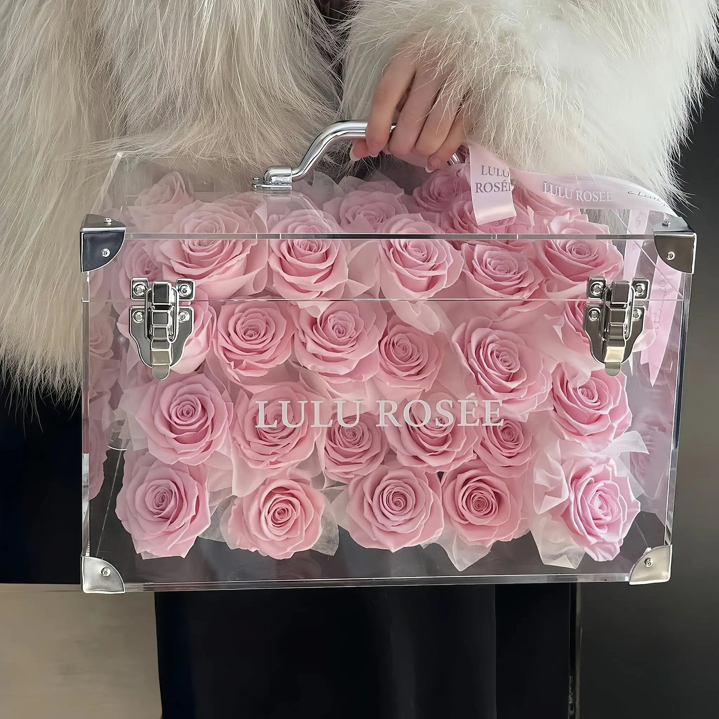 LULU ROSÉE Moyenne Eternal Acrylic Handbag Rose Box, medium transparent acrylic handbag-shaped gift box filled with blush pink preserved roses, soft fur background front full shot, customizable flower colors, elegant everlasting floral gift for birthdays, anniversaries & romantic celebrations