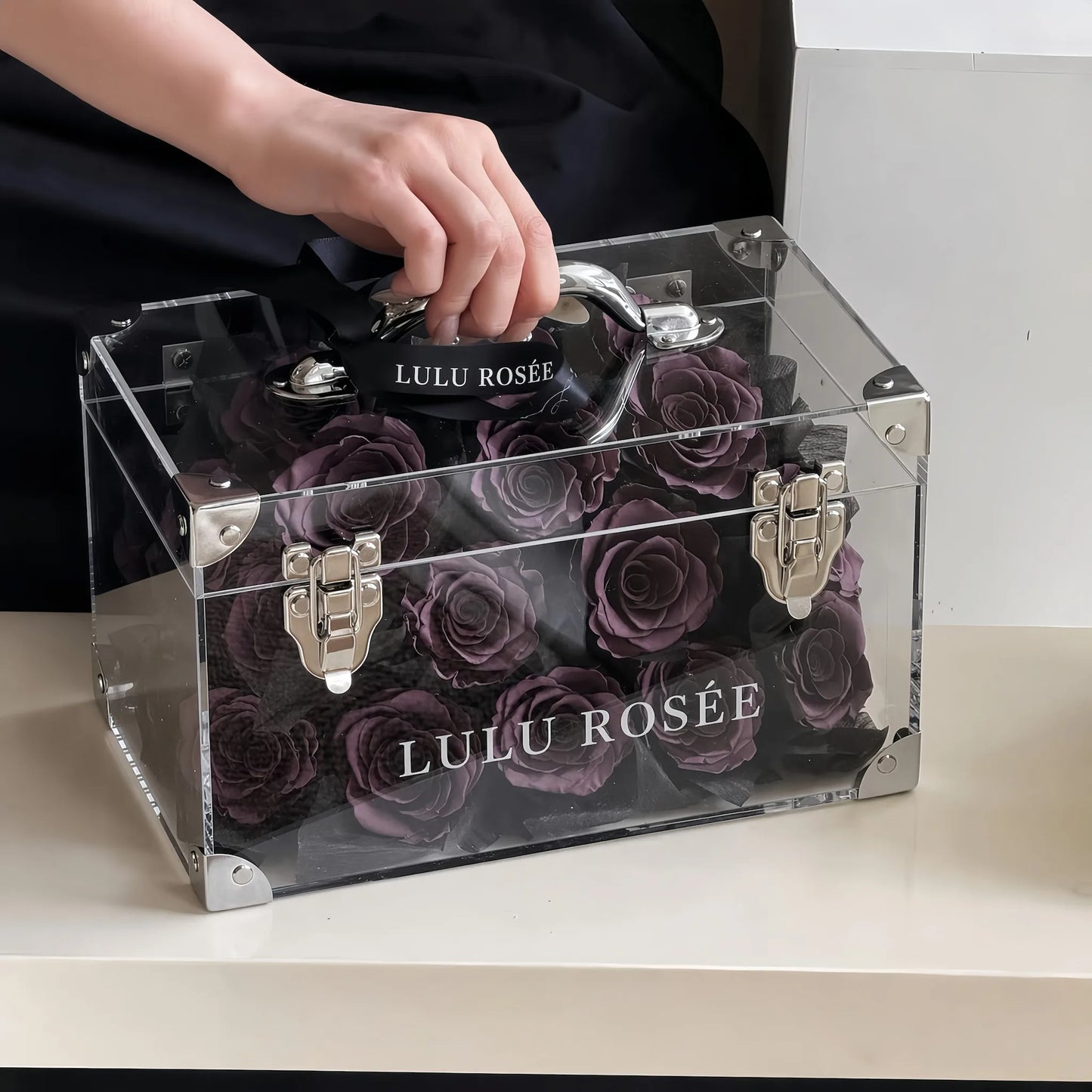 LULU ROSÉE Petite Eternal Acrylic Handbag Rose Box, small transparent acrylic handbag-shaped gift box filled with solid dark purple preserved roses indoor handheld shot, customizable flower color options, mini luxury everlasting floral souvenir for birthday, anniversary & romantic gift giving
