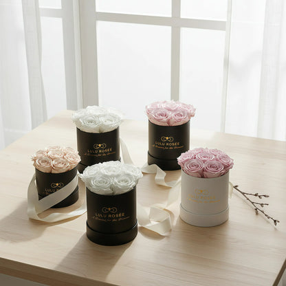 Five black and white round flower boxes with pink and white roses on a light wooden table.
